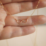Gold infinity necklace being held between fingers